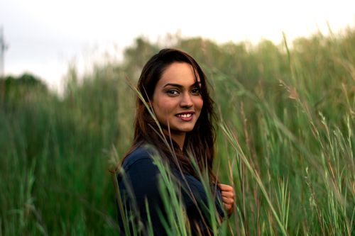 Free Portrait of a smiling woman standing in a lush grass field during the day. Stock Photo