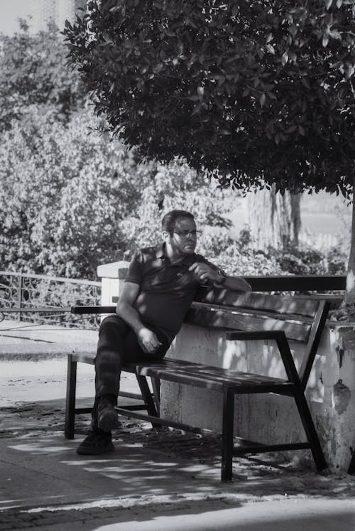 Grayscale Photo of a Man Sitting on a Bench 