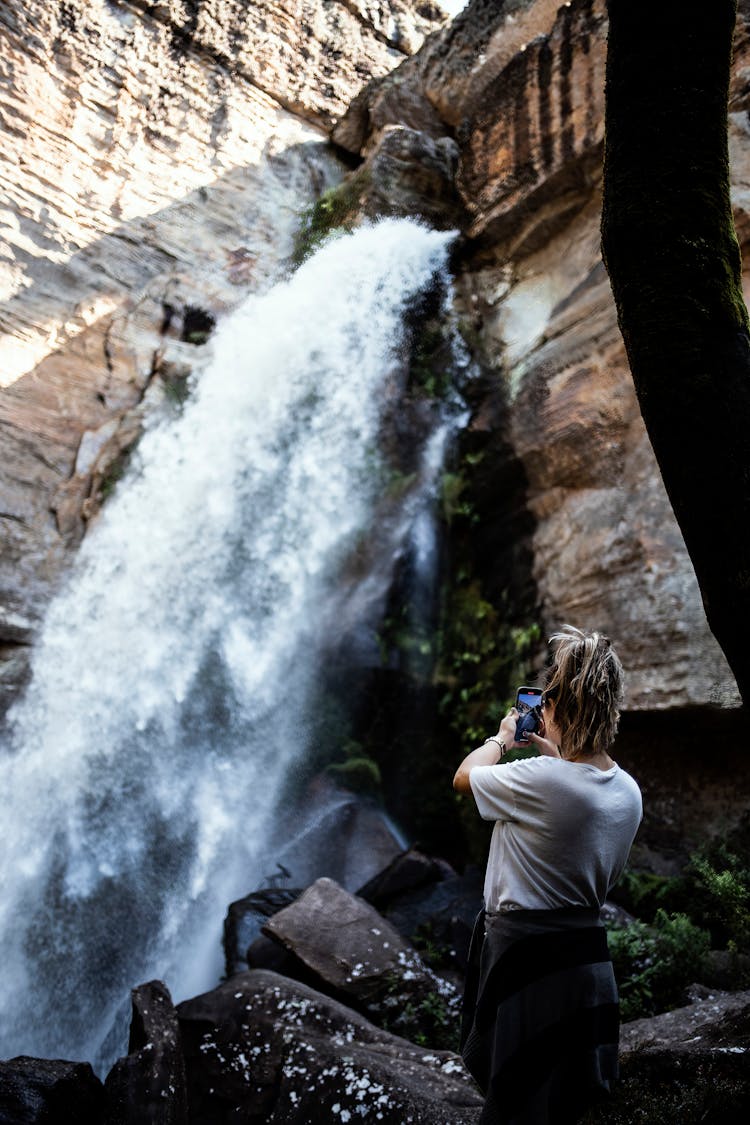 Woman In White Shirt Taking Photo Of Waterfalls