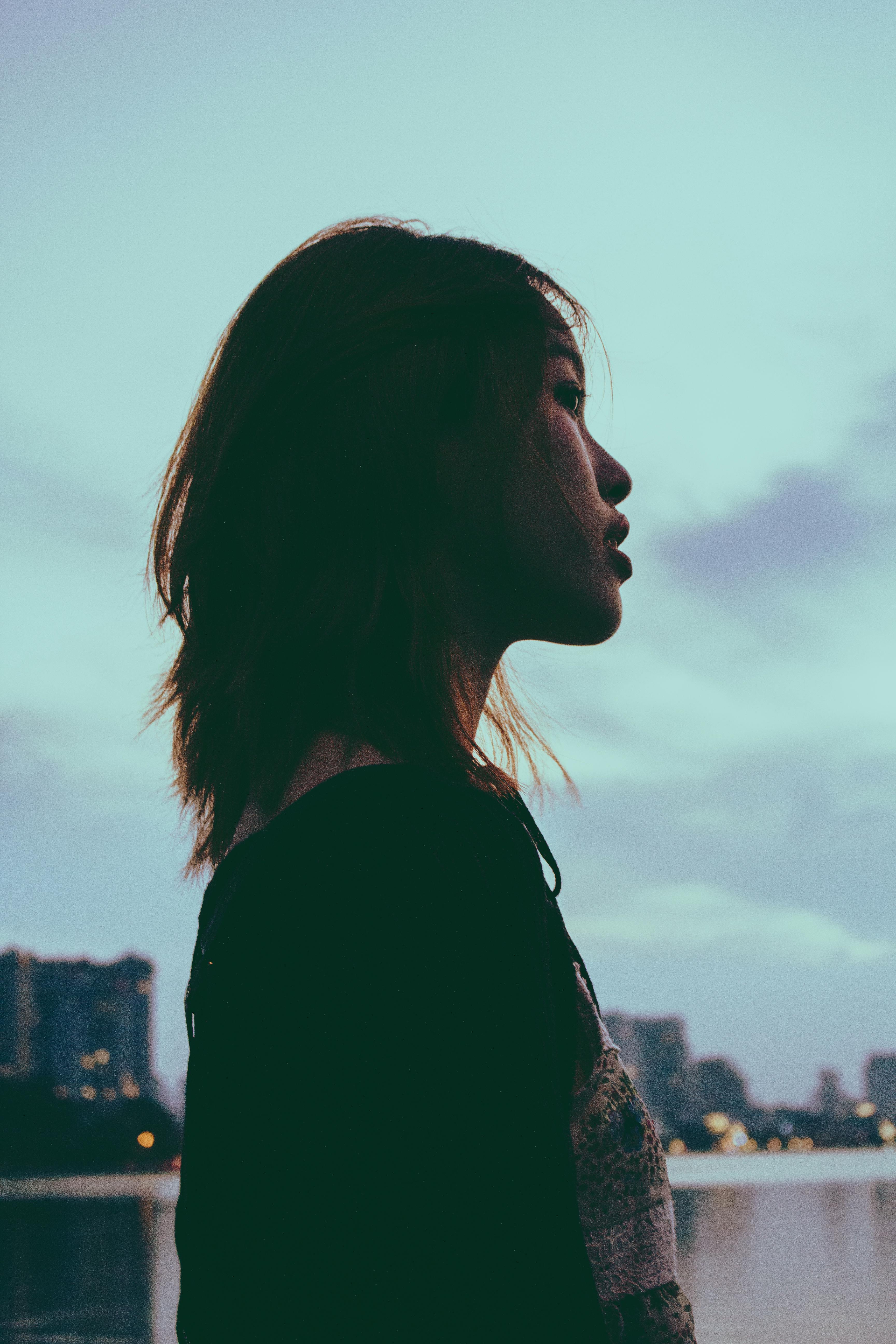 Profile of an Asian woman against a twilight sky, city skyline in background.