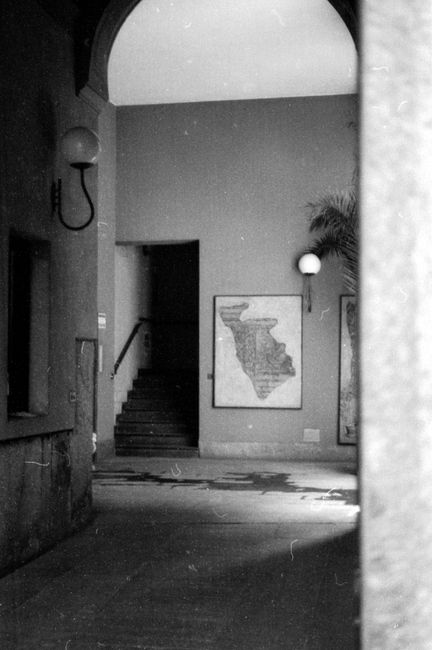 Black and white photograph of a classic interior hallway with arches, stairs, and artwork in Milan, Italy.