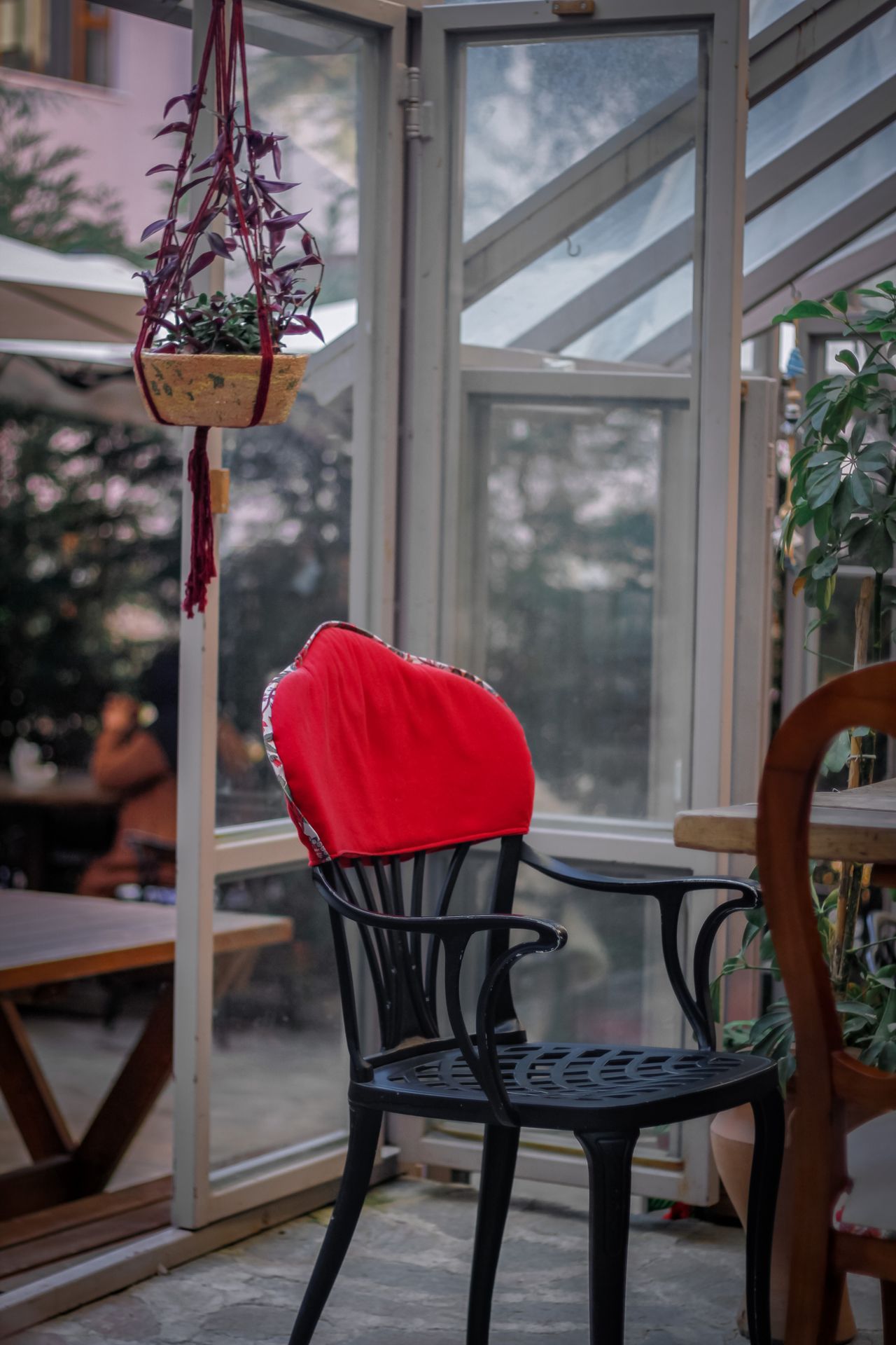 Black metal chair with a red cushion and hanging plant in a glass conservatory