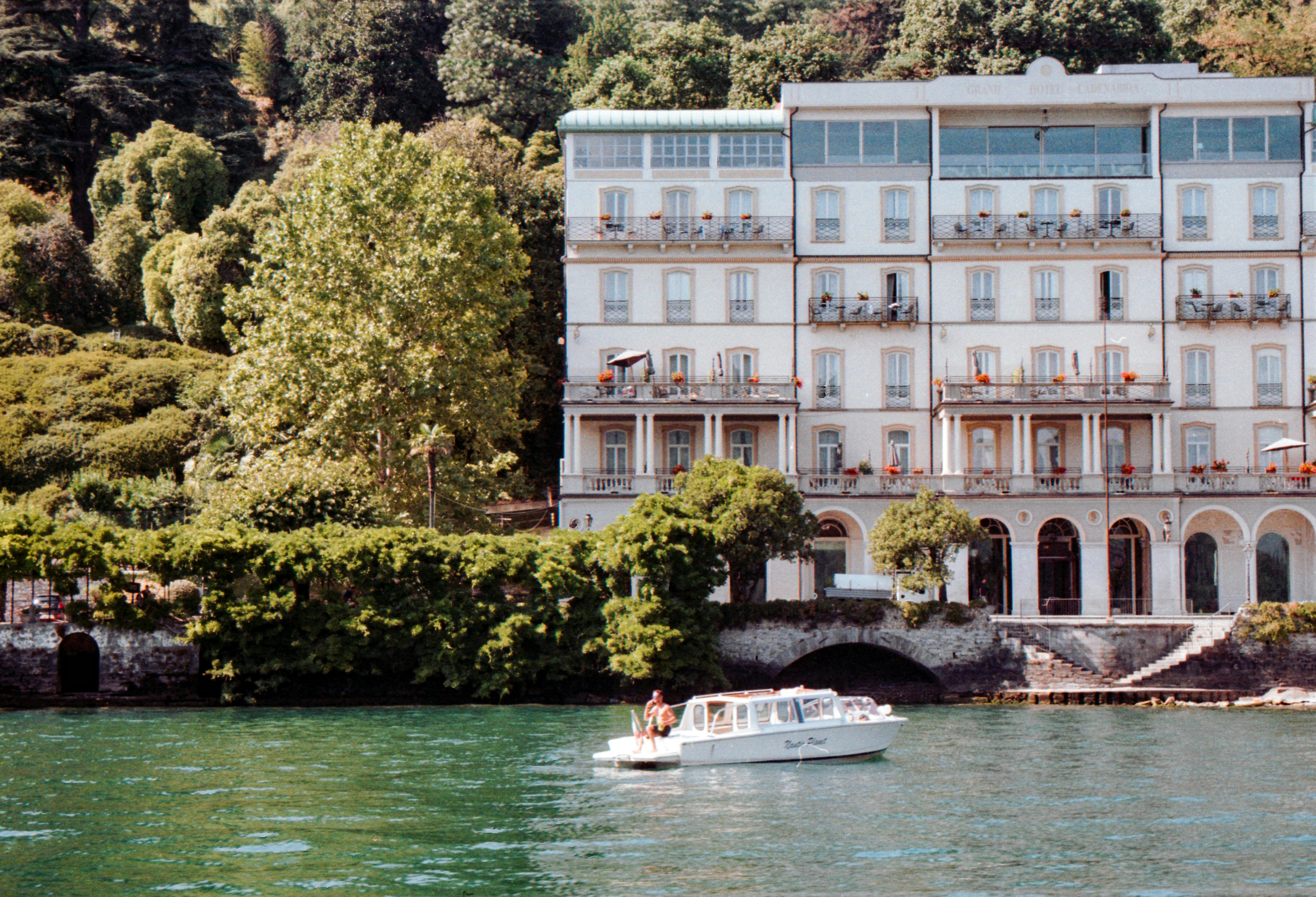 Elegant lakeside hotel with lush greenery and boat, perfect for relaxation and travel.