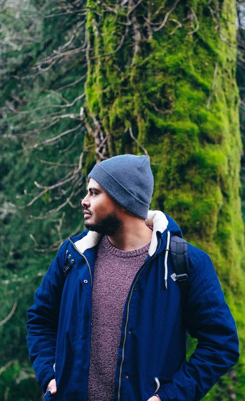 Free Man in blue jacket and beanie exploring a lush, mossy forest on a daytime hike. Stock Photo