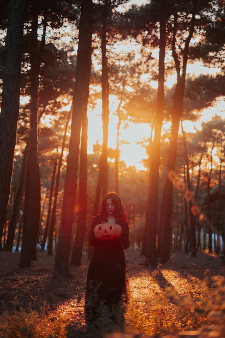 Woman In Black Dress Holding A Carved Pumpkin