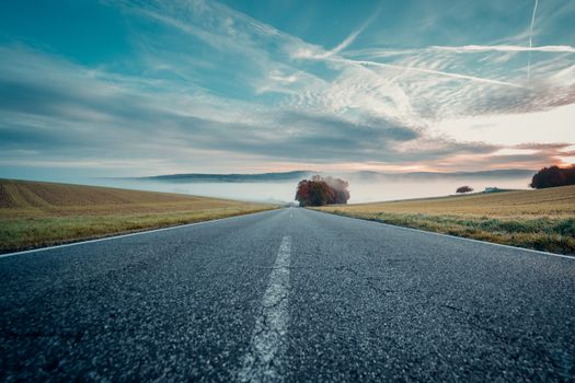 Empty road through fields with a blue sky and morning mist.