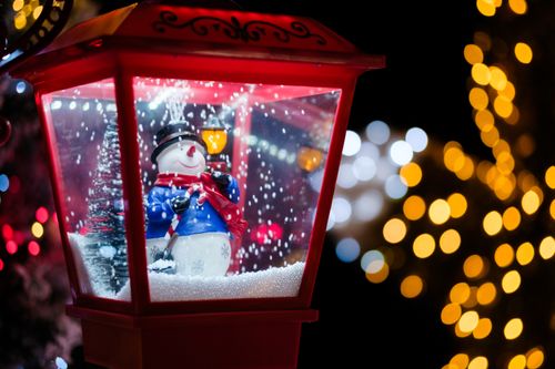 Free Close-up of a snowman in a lantern with glowing Christmas lights, creating a festive winter atmosphere. Stock Photo