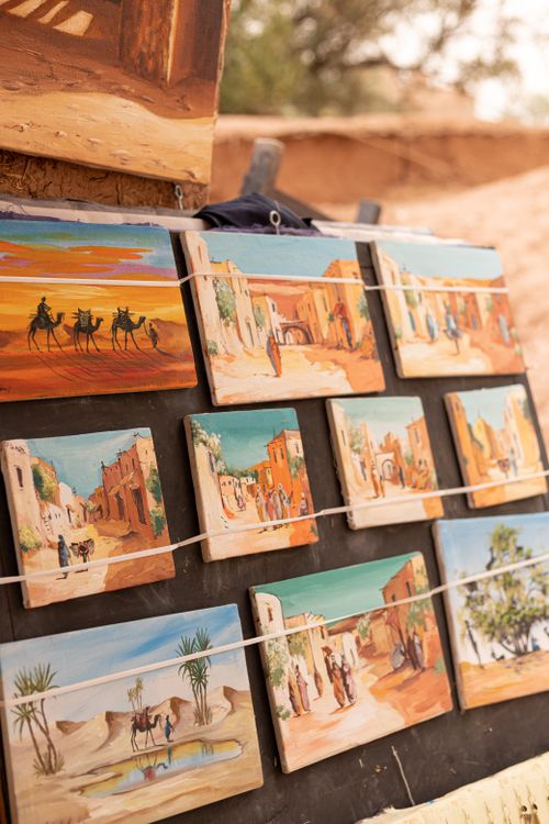 Free A collection of desert-themed paintings on display at an outdoor market, showcasing vibrant desert scenes. Stock Photo