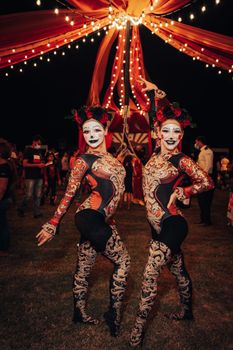 Elegant performers in elaborate costumes at a lively nighttime circus festival.