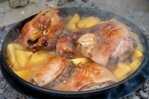 A mouth-watering close-up of braised chicken and pork with potatoes in a hot pan.