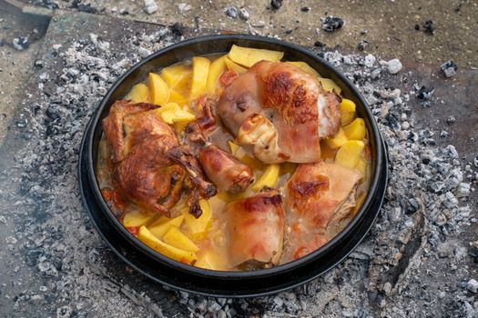 A delicious rustic dish of roasted pork and potatoes cooked outdoors over campfire embers.
