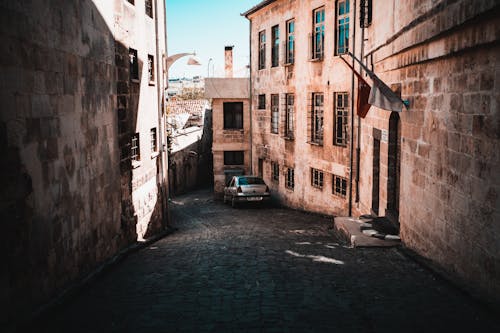 A Car Parked on the Street Between Concrete Buildings