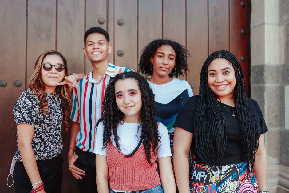 Five friends stand smiling against a wooden door, showcasing diversity and camaraderie.