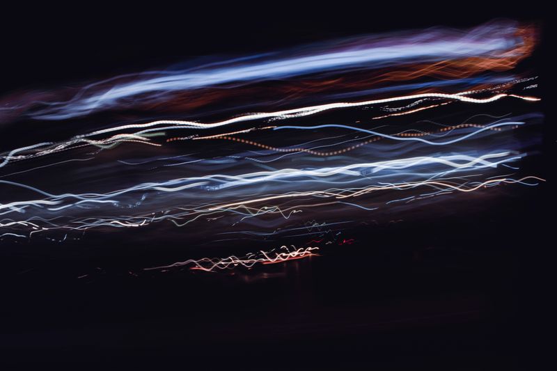 Long-exposure light trails forming pale ribbons across a dark field — photo by Mahdi Bafande on Pexels