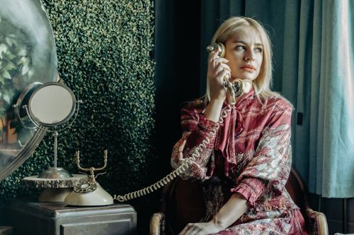 Free A woman in vintage attire uses a rotary phone, evoking retro elegance indoors. Stock Photo