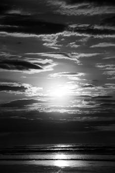 Stunning monochrome view of a dramatic sunrise over the beach with cloudy sky and gentle waves.