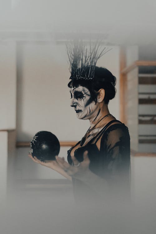 Side View of Woman in Halloween Costume and Makeup Holding a Skull in Her Hand 