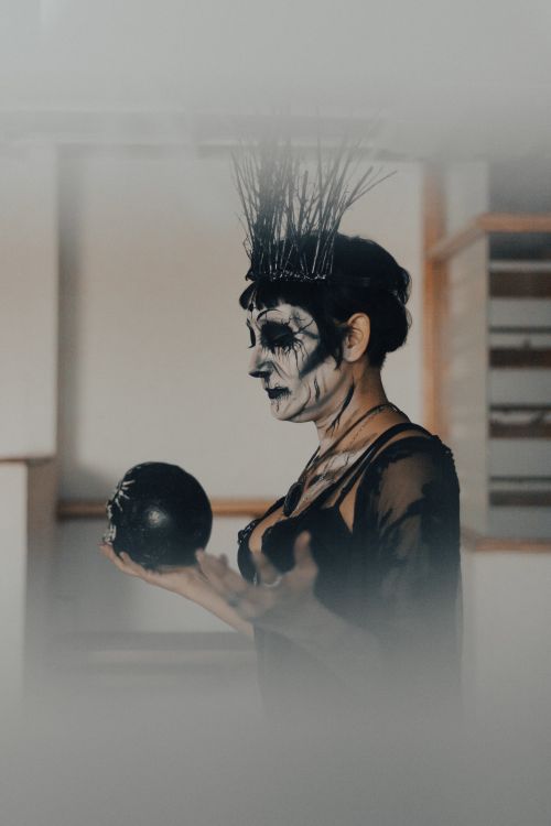 Free Woman in black dress with skull makeup holding a sphere, embodying Halloween spookiness. Stock Photo