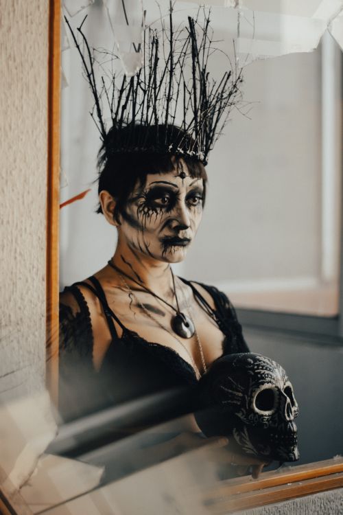 Free A woman with intricate face paint and skull, reflected in a mirror, evokes a Gothic aesthetic. Stock Photo