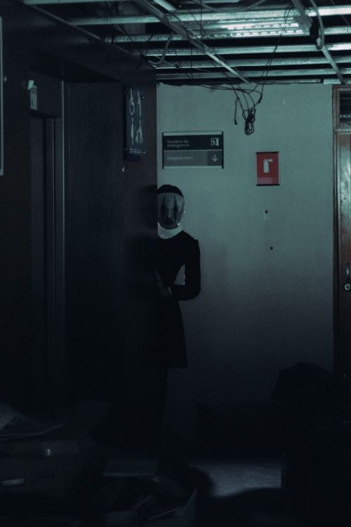 Free A mysterious figure in a mask stands in a dimly lit, abandoned building, creating an eerie atmosphere. Stock Photo