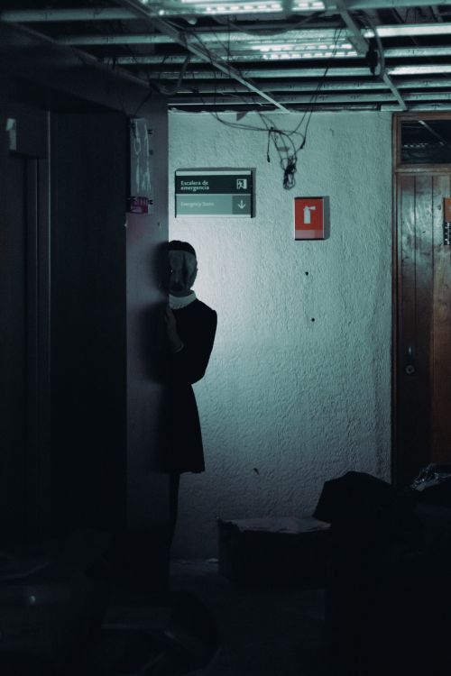 Free A mysterious figure wearing a mask lurks in a dimly lit basement corner, creating a spooky ambiance. Stock Photo
