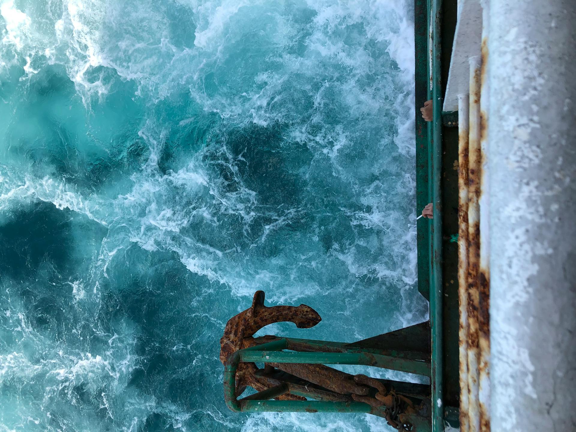 A rusty ship anchor overlooks turbulent sea waves, capturing the essence of maritime adventure.
