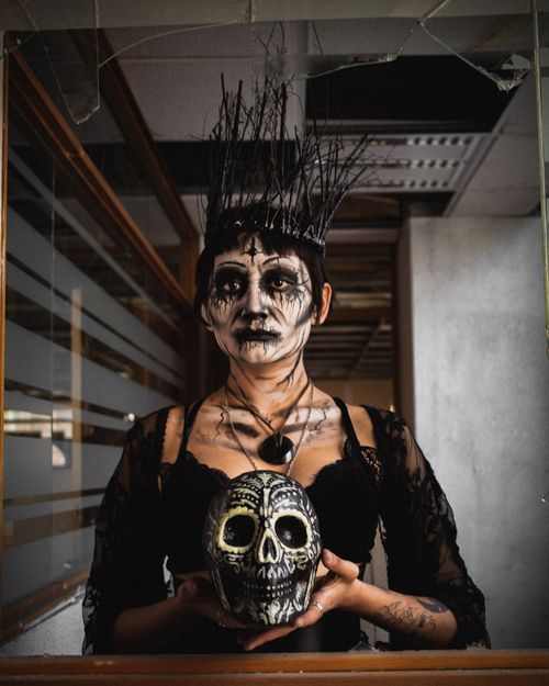 Free Creepy Dia de los Muertos portrait of a woman holding a decorative skull indoors. Stock Photo