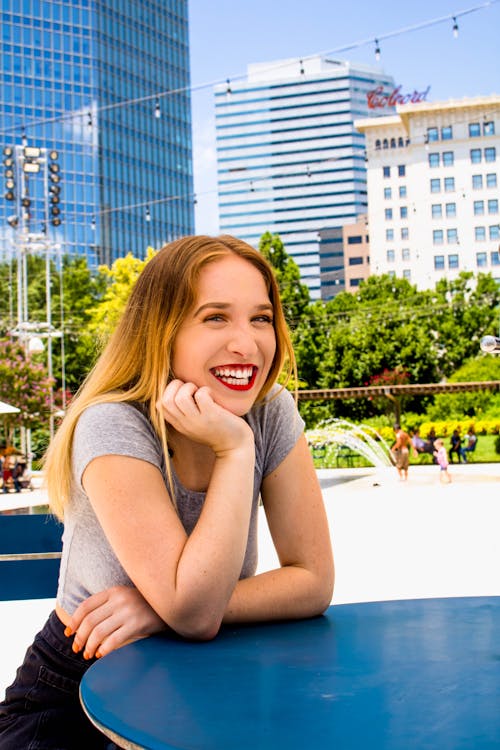 Free Woman Sitting in Front of Blue Table While Smiling on Camera Stock Photo