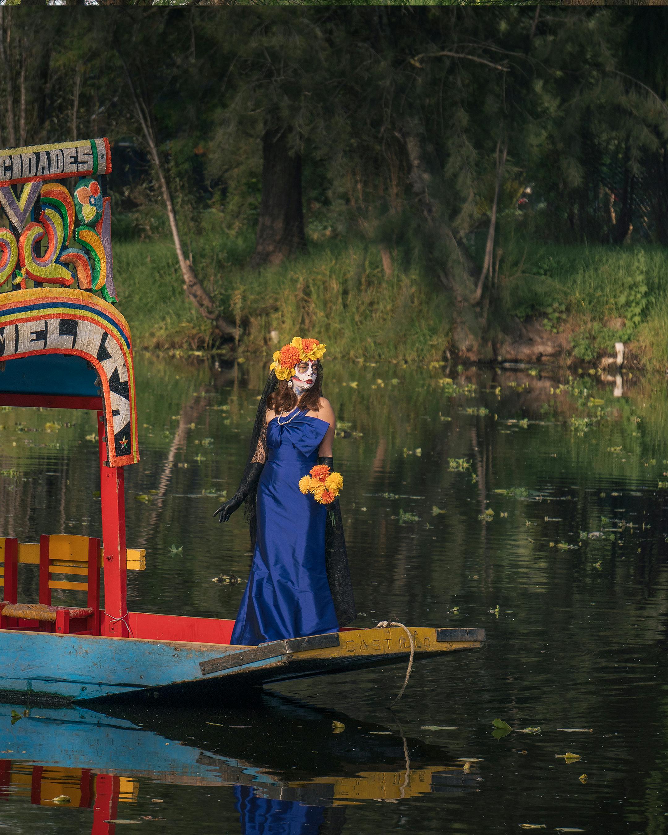 a woman in blue dress standing on a wooden boat at the lake