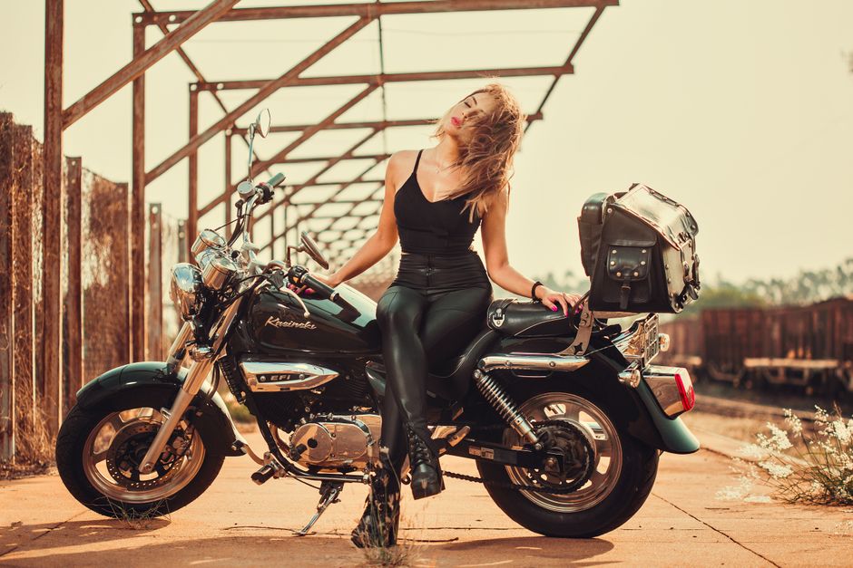 Confident woman in leather posing on a motorcycle under metal arches.