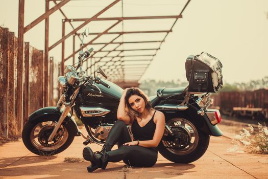 Young woman posing with a motorcycle in an urban environment, exuding confidence and style.