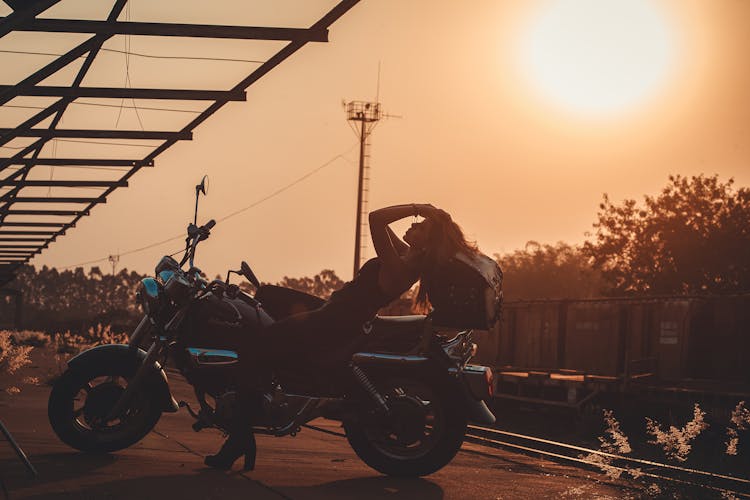 Silhouette Of A Woman Lying On The Motorcycle Seat During Sunset