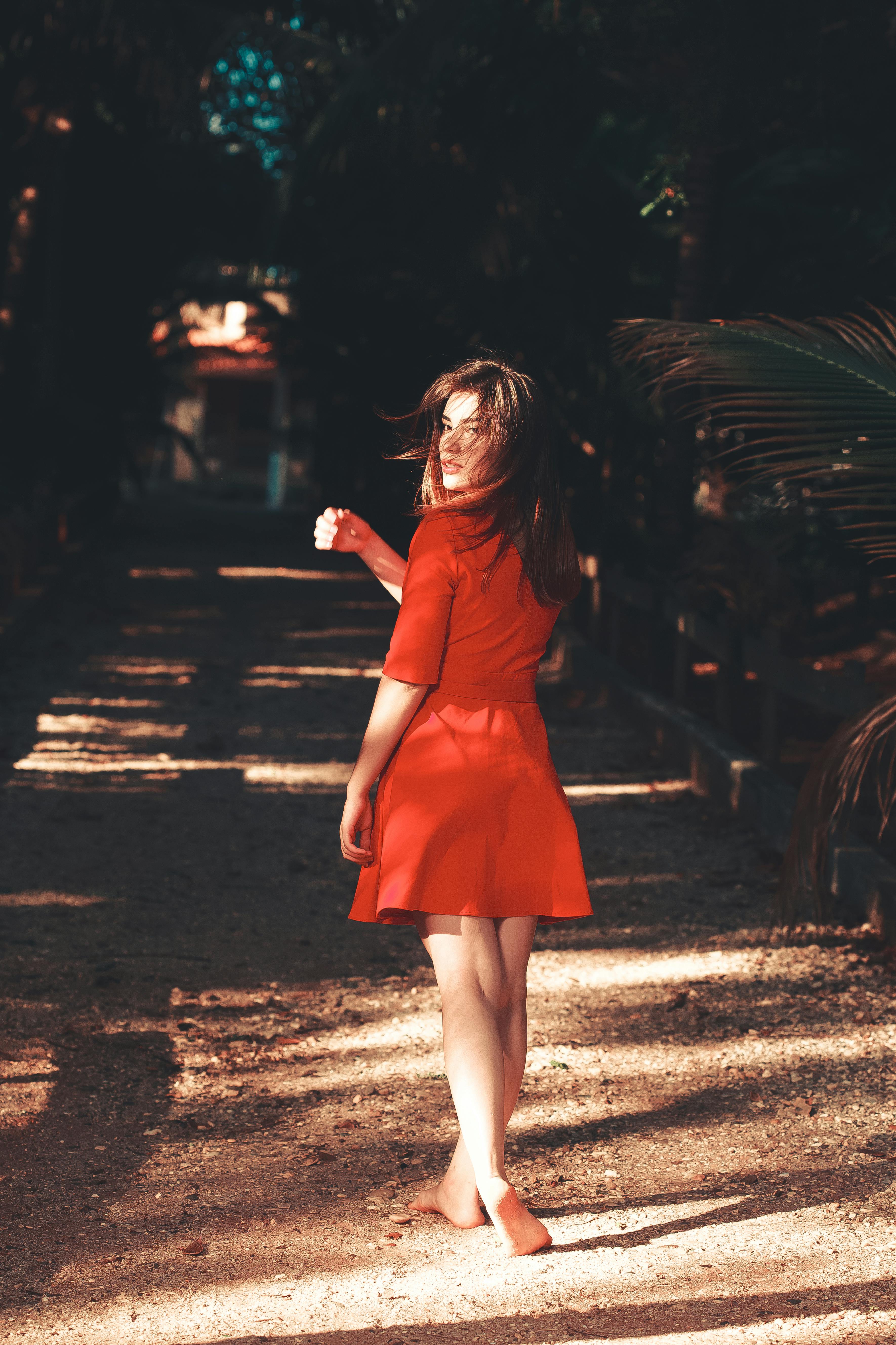 Free Woman in a red dress walking barefoot on a sunlit path during summer. Stock Photo