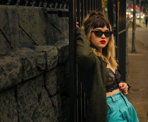 A Woman Wearing a Green Coat and Black Bra Leaning on a Metal Gate