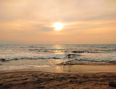 Peaceful beach scene during sunset with gentle waves and warm tones.