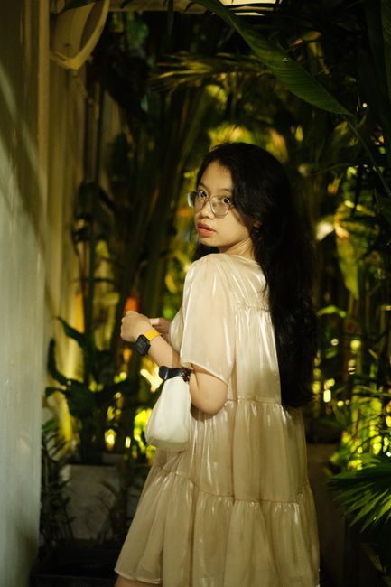 Stylish young woman in glasses posing at night in a lush garden setting.