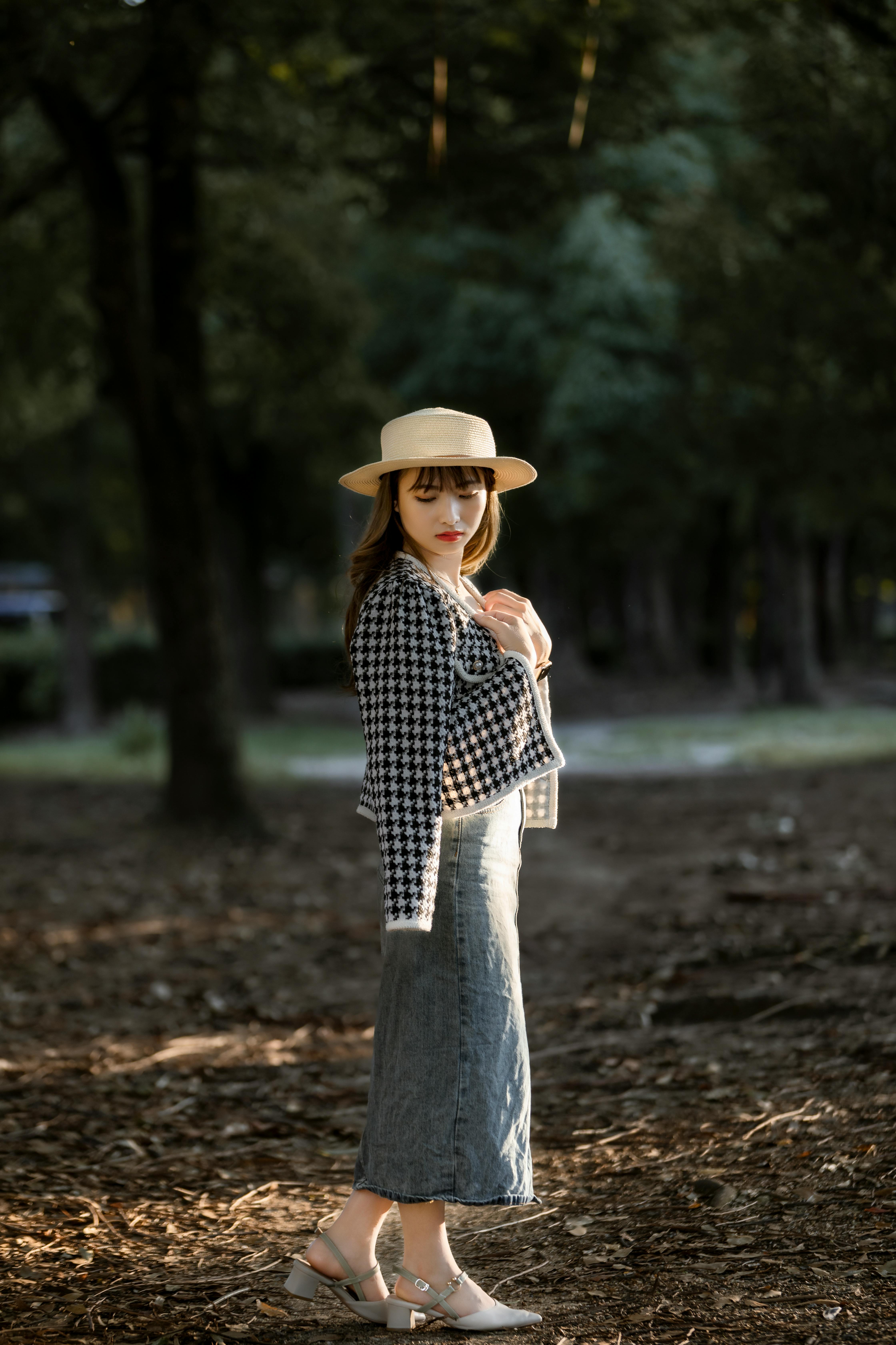 Fashionable woman in a brown hat posing stylishly in a serene park setting.