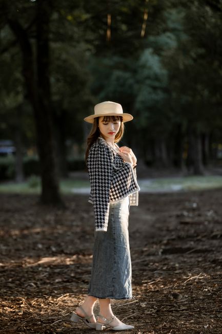 Fashionable woman in a brown hat posing stylishly in a serene park setting.