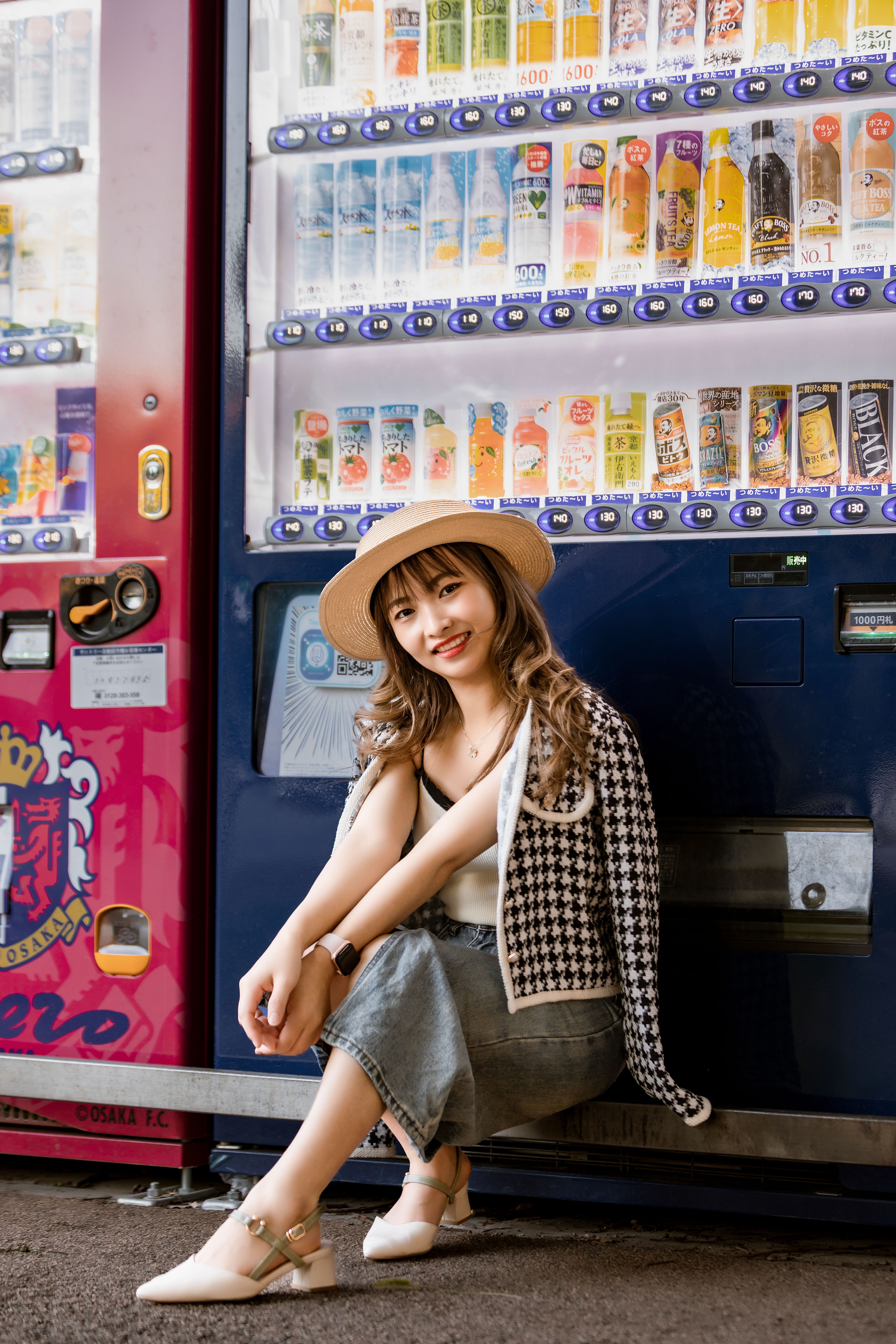 Chic young woman smiling by a colorful vending machine, showcasing modern fashion and style.