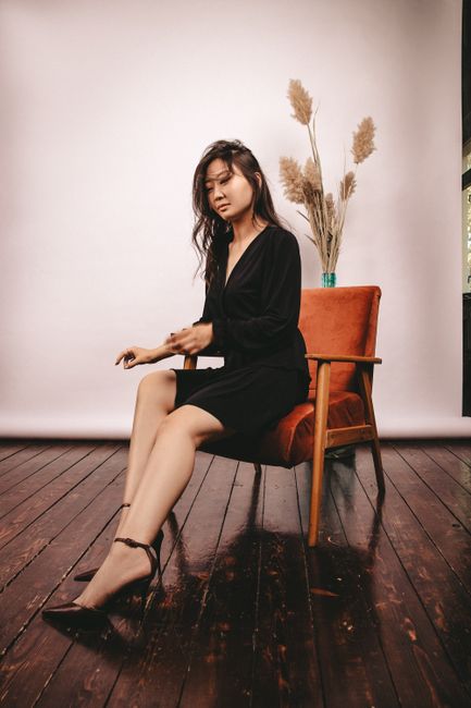 Stylish woman in black dress sitting indoors, exuding elegance and poise.