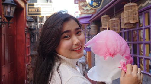 Young Woman Walking with a Pink Cotton Candy in Hand and Looking over Shoulder 