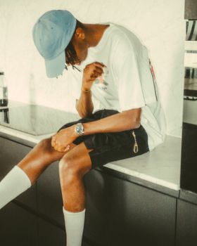 Fashionable young man in a blue cap sitting on a modern kitchen counter indoors.