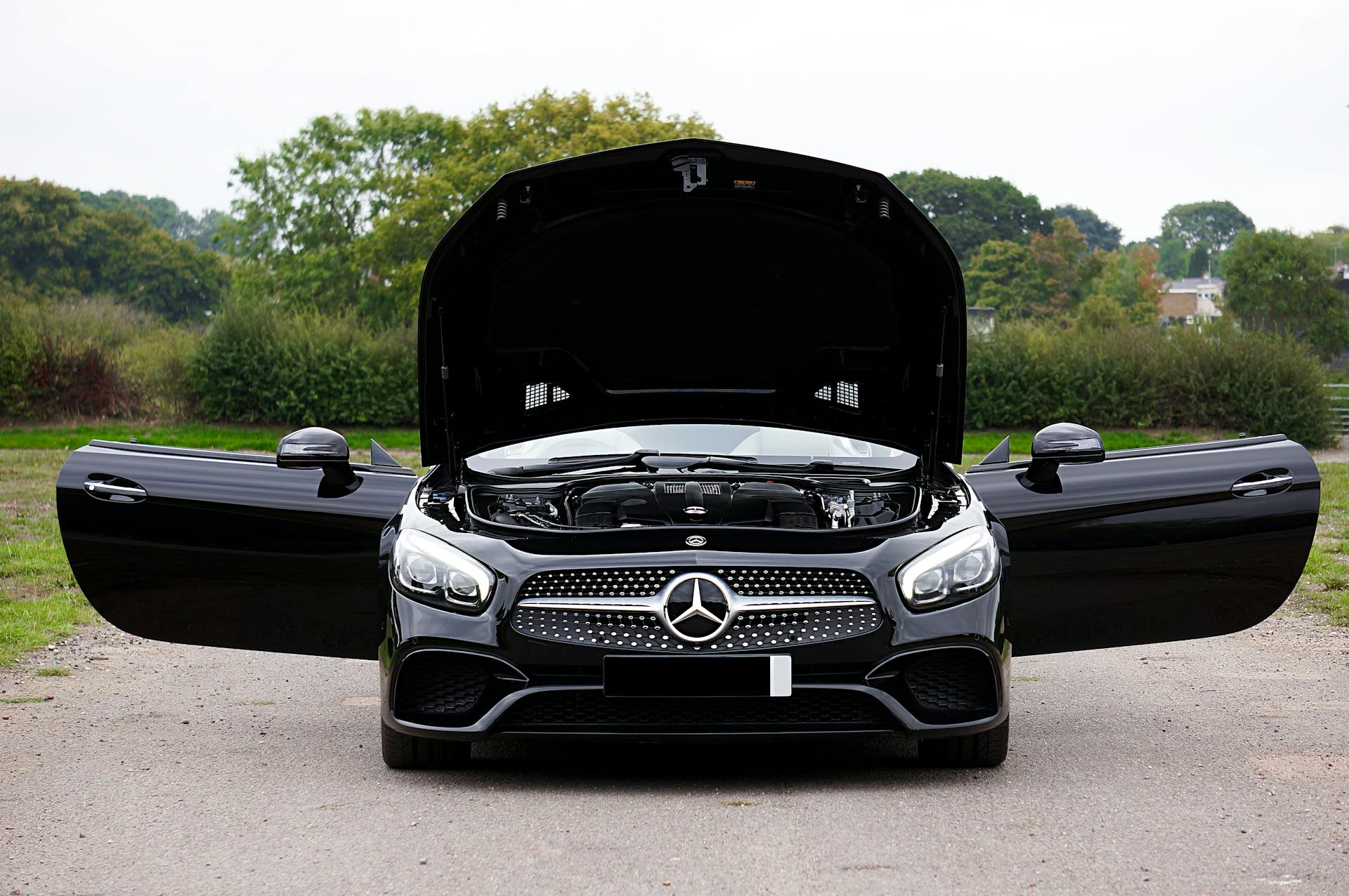 Front view of a black Mercedes-Benz AMG with opened doors and hood, showcasing its engine.