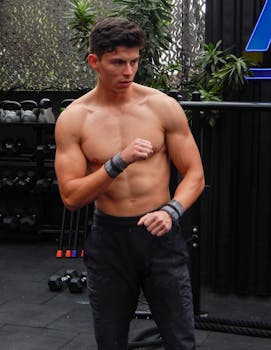 Athletic shirtless man practicing boxing moves outdoors at gym.