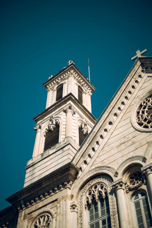 Free Low-angle view of a Gothic Revival church tower with ornate details and a clear blue sky background. Stock Photo