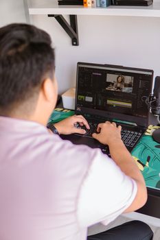 Man editing video on laptop in home workspace with tropical-themed desk mat.