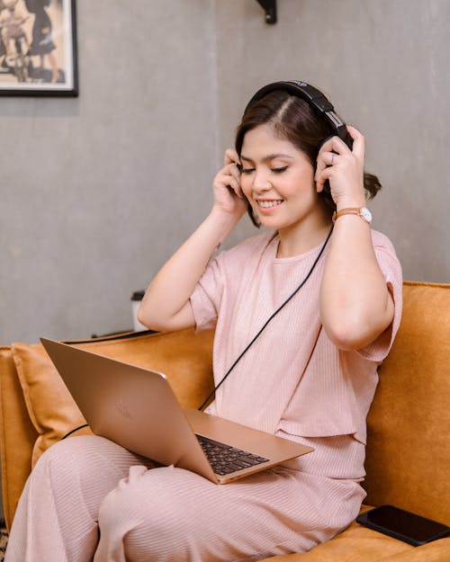 Young Woman Sitting on a Sofa with a Laptop and Wearing Headphones