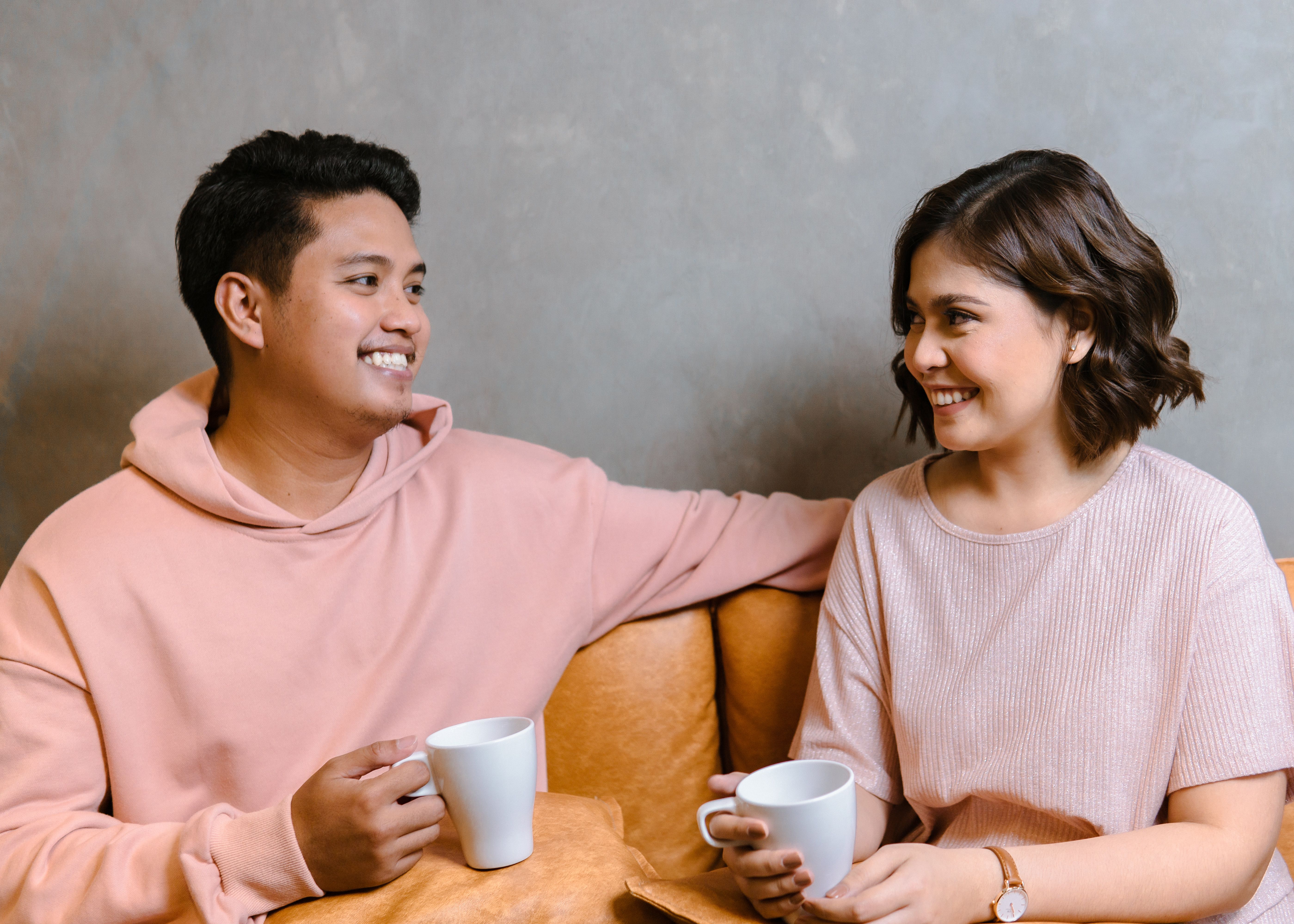 Two friends laughing together over hot drinks outdoors, at the blurry line between close friendship and something more