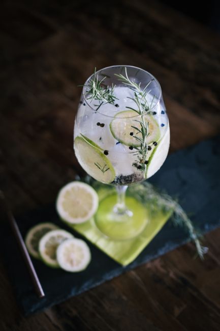 A tall glass of gin and tonic over ice, garnished with a lime wedge, condensation beading on the outside of the glass.