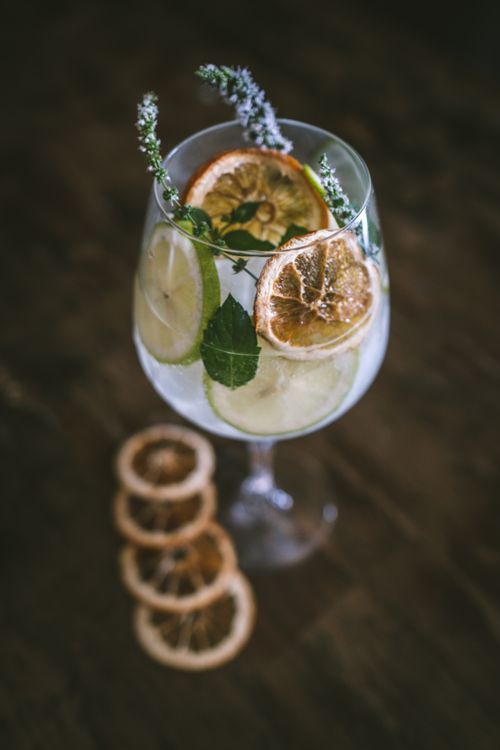 Free Elegant cocktail garnished with lime, dried lemon slices, and fresh herbs, perfect for summer refreshment. Stock Photo